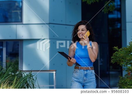 Successful beautiful business woman in suit with document walking to the meeting near modern office building. Successful beautiful business woman in suit with document walking to the meeting near modern office building. 95608103