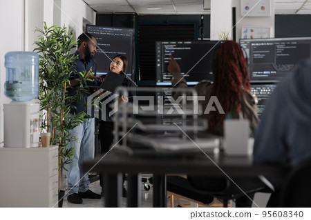 Engineers checking artificial intelligence code looking for errors on laptop, checking big tv monitor in it agency office. Programmers working on cyber security innovation in busy software company Engineers checking artificial intelligence code looking for errors on laptop, checking big tv monitor in it agency office. Programmers working on cyber security innovation in busy software company 95608340