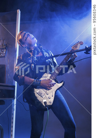Female punk rocker singing rock at guitar with microphone, doing live performance and feeling heavy metal music in studio. Performing alternative rock song and being ecstatic about solo concert. Female punk rocker singing rock at guitar with microphone, doing live performance and feeling heavy metal music in studio. Performing alternative rock song and being ecstatic about solo concert. 95608346