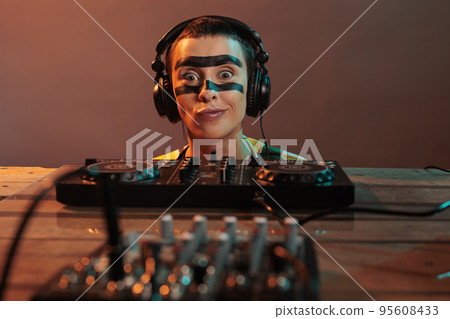 Young performer acting funky looking at mixer, being focused on control buttons at dj turntables over background. Looking closely at audio equipment to mix techno music, stereo instrument. 95608433