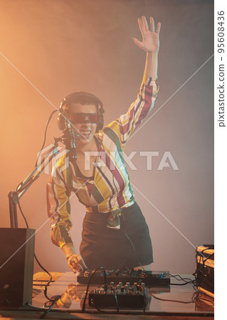Cool disc jockey using mixer to play techno at party, mixing music on dj turntables with electric keys in studio. Young artist with headphones and microphone playing remix with control buttons. 95608436