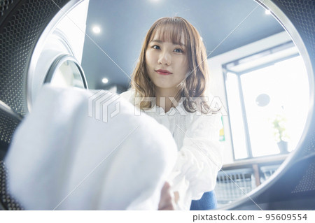 Young woman doing laundry in a coin laundry Young woman doing laundry in a coin laundry 95609554