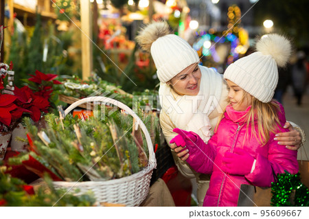 Cheerful girl with mom choosing New Year tree Cheerful girl with mom choosing New Year tree 95609667