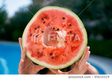 Girl sends a kiss through a cut hole in a slice of watermelon holding it in her hands. High quality photo Girl sends a kiss through a cut hole in a slice of watermelon holding it in her hands. High quality photo 95610329