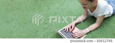 Smiling blonde woman working on laptop lay on grass, remote job, female freelancer outdoors Smiling blonde woman working on laptop lay on grass, remote job, female freelancer outdoors 95612749