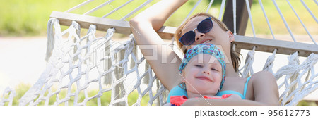 Resting mother embrace daughter, girls lay on hammock in shadow, enjoy life, time with family Resting mother embrace daughter, girls lay on hammock in shadow, enjoy life, time with family 95612773