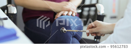 Doctor neurologist checking knee reflexes of female patient with percussion hammer in clinic 95612783