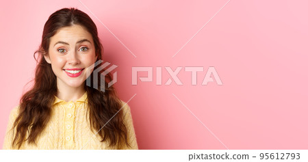 Close up of cute brunette lady smiles at camera, trying to make friendly and polite face, stands against pink background Close up of cute brunette lady smiles at camera, trying to make friendly and polite face, stands against pink background 95612793