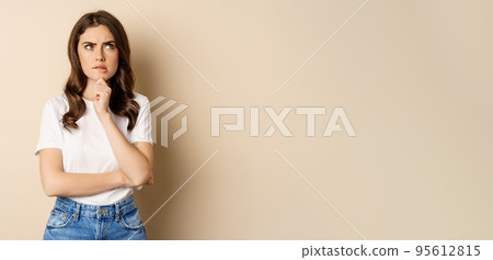 Portrait of serious woman thinking, looking up with indecisive thoughtful face, pondering, standing over beige background 95612815