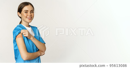 Female nurse, doctor medical worker got vaccinated, showing shoulder with patch after covid-19 vaccine, smiling pleased, standing over white background Female nurse, doctor medical worker got vaccinated, showing shoulder with patch after covid-19 vaccine, smiling pleased, standing over white background 95613086