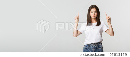 Sulking timid girl pointing fingers up, feeling upset 95613159