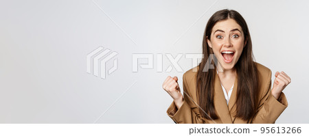 Enthusiastic girl screaming and rejoicing, looking at camera, winning, celebrating victory and triumphing, standing over white background 95613266
