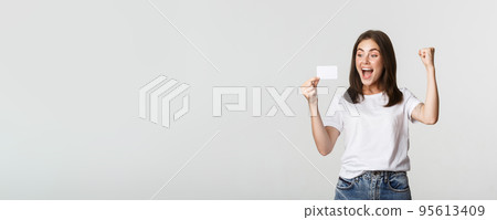 Joyful good-looking girl rejoicing and looking at credit card, fist pump while triumphing, white background Joyful good-looking girl rejoicing and looking at credit card, fist pump while triumphing, white background 95613409
