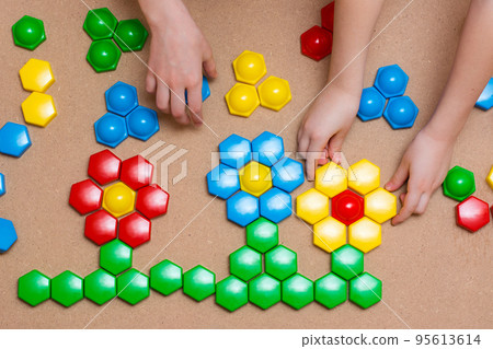 Children's pens folded the details of the colored mosaic into a pattern of flowers on the table. Leisure time for a child in quarantine. Board game. View from above 95613614