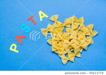 Raw farfale pasta and the word "pasta" on a blue cardboard background. Top view 95613778