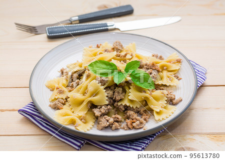 Ready-to-eat pasta navy with minced meat and basil leaves on a plate and cutlery on a wooden table. Russian cuisine 95613780