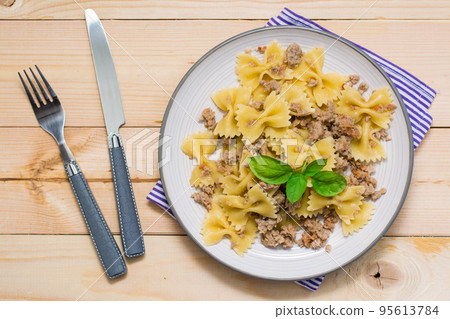 Ready-to-eat pasta navy with minced meat and basil leaves on a plate and cutlery on a wooden table. Russian cuisine. Top view 95613784
