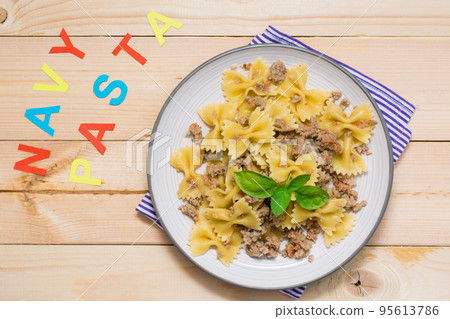 Ready-to-eat pasta navy with minced meat and basil leaves on a plate and the word "pasta navy" from colored letters on a wooden table. Russian cuisine. Top view 95613786