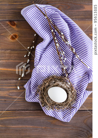Happy easter. One white chicken egg in a bird's nest and willow branches on a wooden table. Rustic style. Copy space. Top view Happy easter. One white chicken egg in a bird's nest and willow branches on a wooden table. Rustic style. Copy space. Top view 95613885