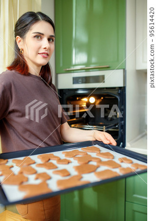 Young smiling mixed race woman preparing homemade cookies for breakfast. Selective focus, vertical 95614420