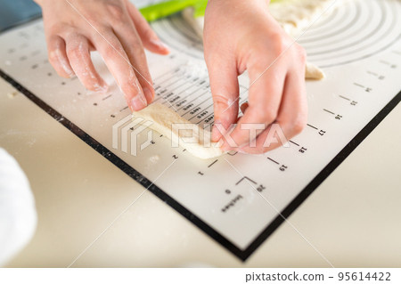Close-up of a cook's hands measuring out equal 4-inch pieces of dough using a marked baking mat 95614422