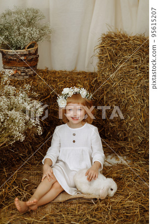 A cute and beautiful little girl is sitting in the hayloft with a rabbit A cute and beautiful little girl is sitting in the hayloft with a rabbit 95615207