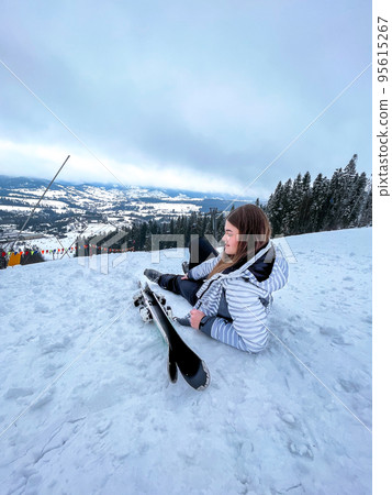 Shot of a skier woman sitting on the ski slope resting relaxing extreme recreation active lifestyle activity. Female skier on a slope in the mountains. Winter active sport Shot of a skier woman sitting on the ski slope resting relaxing extreme recreation active lifestyle activity. Female skier on a slope in the mountains. Winter active sport 95615267