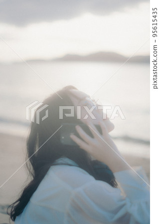 Photo of a woman making a phone call on the beach Photo of a woman making a phone call on the beach 95615435