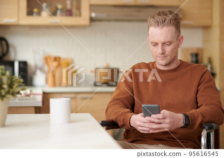 Young man with disability drinking morning coffee and reading news on smartphone Young man with disability drinking morning coffee and reading news on smartphone 95616545