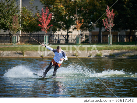 Wakeboarder surfing on lake. Young man surfer having fun wakeboarding in the cable park. Water sport, outdoor activity concept. 95617148