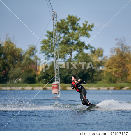 Wakeboarder surfing on lake. Young man surfer having fun wakeboarding in the cable park. Water sport, outdoor activity concept. 95617157