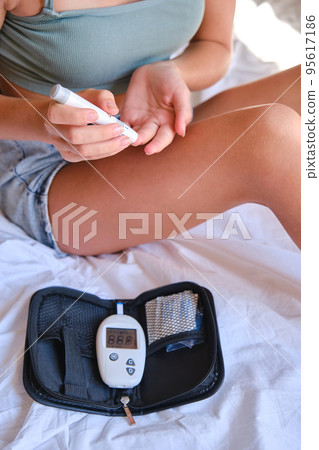 The girl measures the level of glucose in the blood on the bed at home. The girl measures the level of glucose in the blood on the bed at home. 95617186