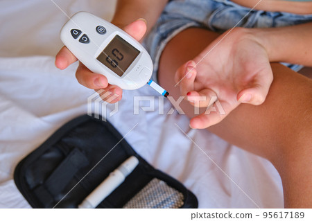 Teenager with diabetes measures blood glucose levels with a glucometer on the bed at home. 95617189