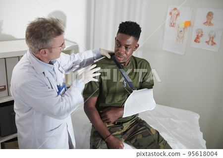 Surgeon examining military man with broken arm in medical office Surgeon examining military man with broken arm in medical office 95618004