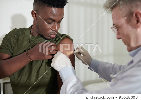 Doctor sticking band aid on injection spot on shoulder of military man Doctor sticking band aid on injection spot on shoulder of military man 95618008