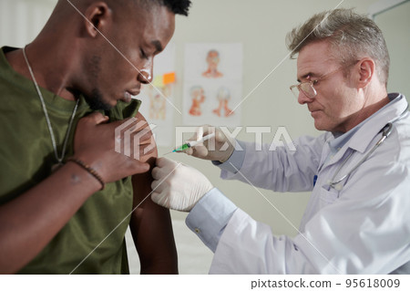 Medical worker injecting vaccine against coronavirus in soulder of Black soldier Medical worker injecting vaccine against coronavirus in soulder of Black soldier 95618009