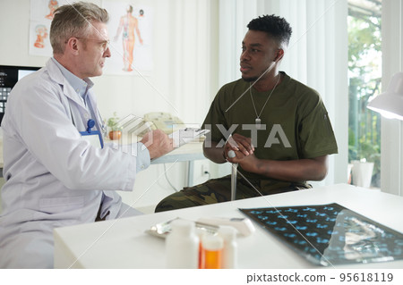 Doctor writing down complains when talking to ex-soldier in medical office Doctor writing down complains when talking to ex-soldier in medical office 95618119