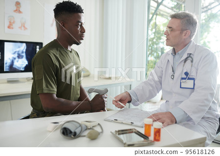 Doctor asking ex-soldier to fill health insurance document before check-up Doctor asking ex-soldier to fill health insurance document before check-up 95618126