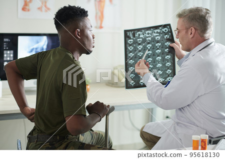 Doctor talking to military man about back pain and showing spine discs MRI image that helps to track recovery Doctor talking to military man about back pain and showing spine discs MRI image that helps to track recovery 95618130