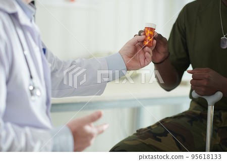 Cropped image of doctor giving container with pills to ex-soldier Cropped image of doctor giving container with pills to ex-soldier 95618133