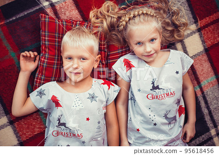Top view of little blonde girl and boy in christmas pajamas lying on checkered blanket and pillows  95618456