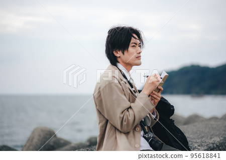 A man sitting on the breakwater and taking notes 95618841