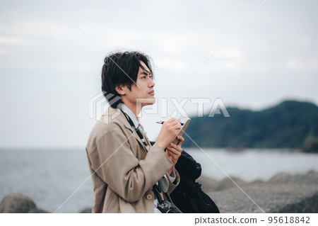 A man sitting on the breakwater and taking notes A man sitting on the breakwater and taking notes 95618842