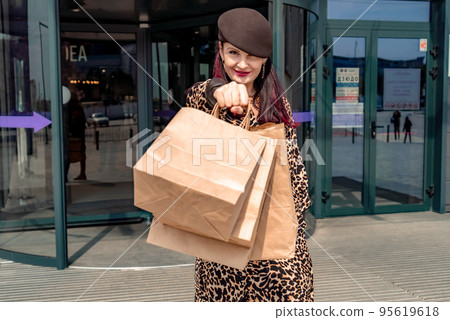 A happy shopaholic girl keeps her bags near the shopping center. A woman near the store is happy with her purchases, holding bags. Dressed in a leopard print dress. Consumer concept. A happy shopaholic girl keeps her bags near the shopping center. A woman near the store is happy with her purchases, holding bags. Dressed in a leopard print dress. Consumer concept. 95619618