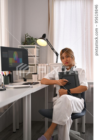 Portrait of young creative woman sitting front of computer in modern home office and smiling to camera Portrait of young creative woman sitting front of computer in modern home office and smiling to camera 95619846