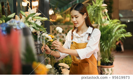Female florist wearing apron arranging flowers at her rustic flower shop. Business, sale and floristry concept Female florist wearing apron arranging flowers at her rustic flower shop. Business, sale and floristry concept 95619973