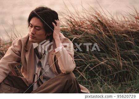 黃昏時坐在草地上的男人 95620729