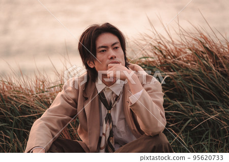 黃昏時坐在草地上的男人 95620733