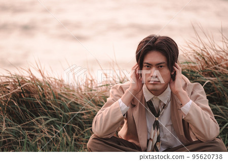 黃昏時坐在草地上的男人 95620738