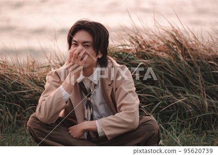 黃昏時坐在草地上的男人 95620739